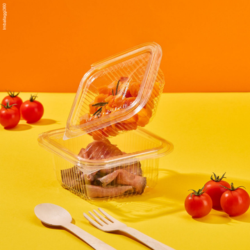 Vaschette trasparenti per gastronomia, mostrate aperta e piene di cibo. Pomodorini sparsi tutto su sfondo giallo